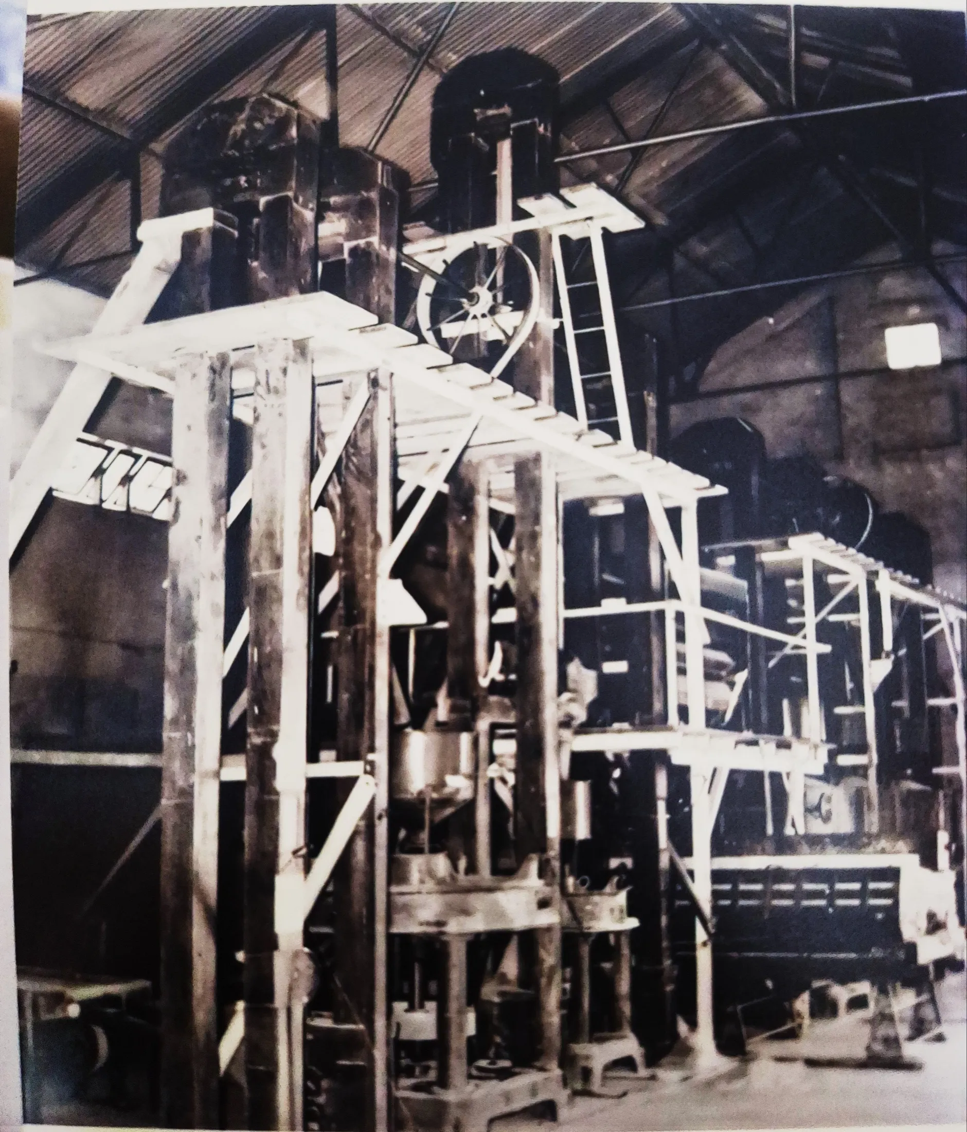 A multi-storey milling tower of riveted steel and timber staging, under the trusses of a shed roof.