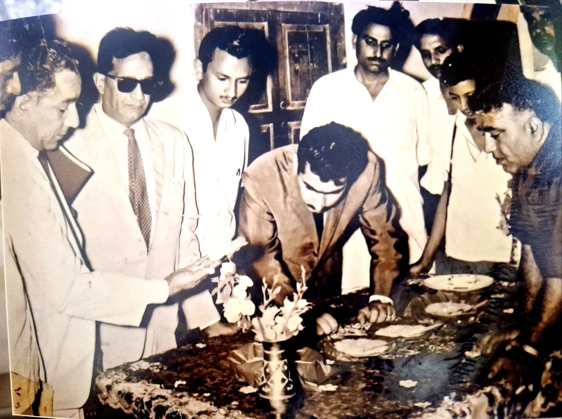 Men grade trays of rice at a table; the founder leans in to inspect a sample.