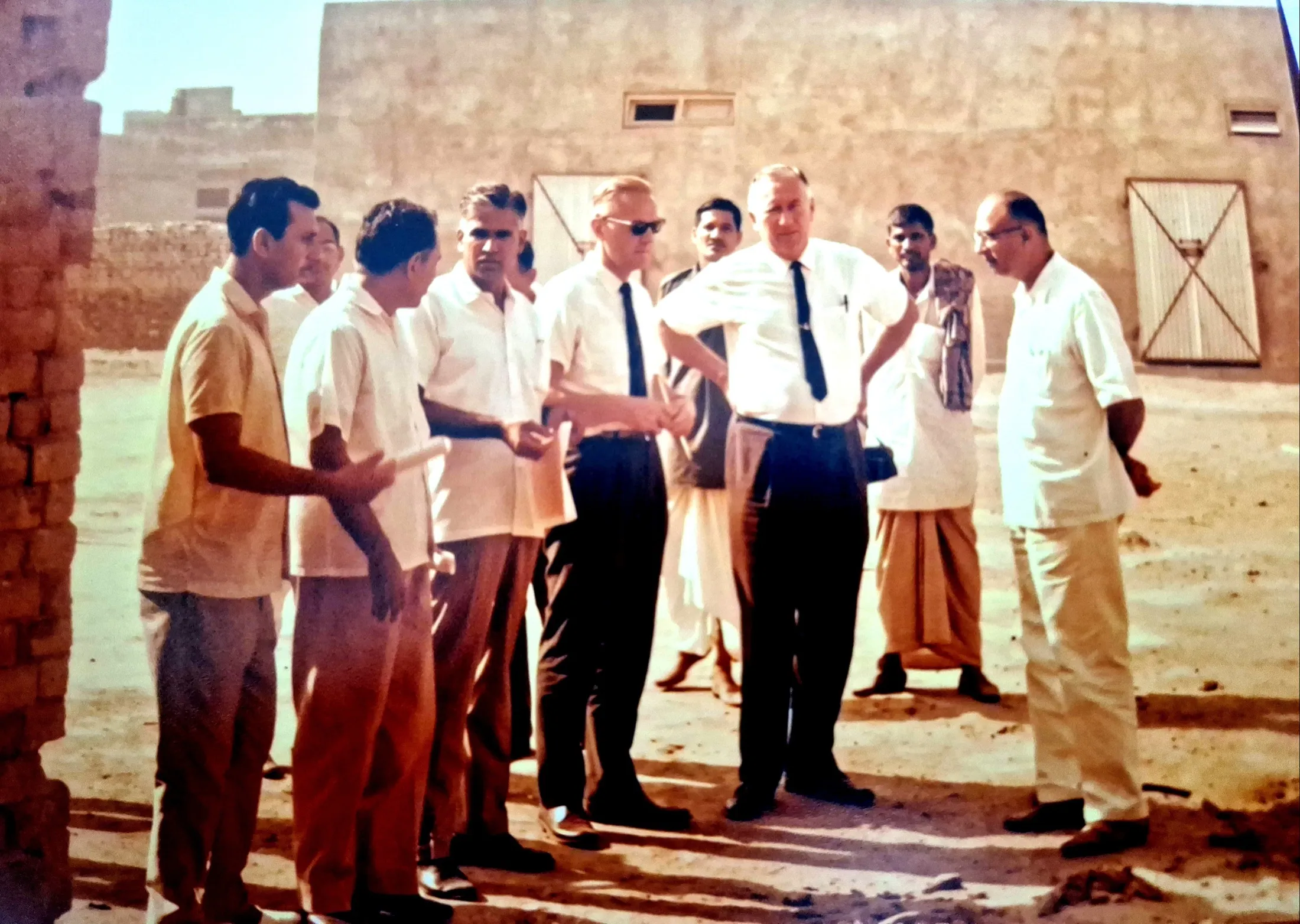 On site outdoors, two foreign visitors and the management team discuss the next building.